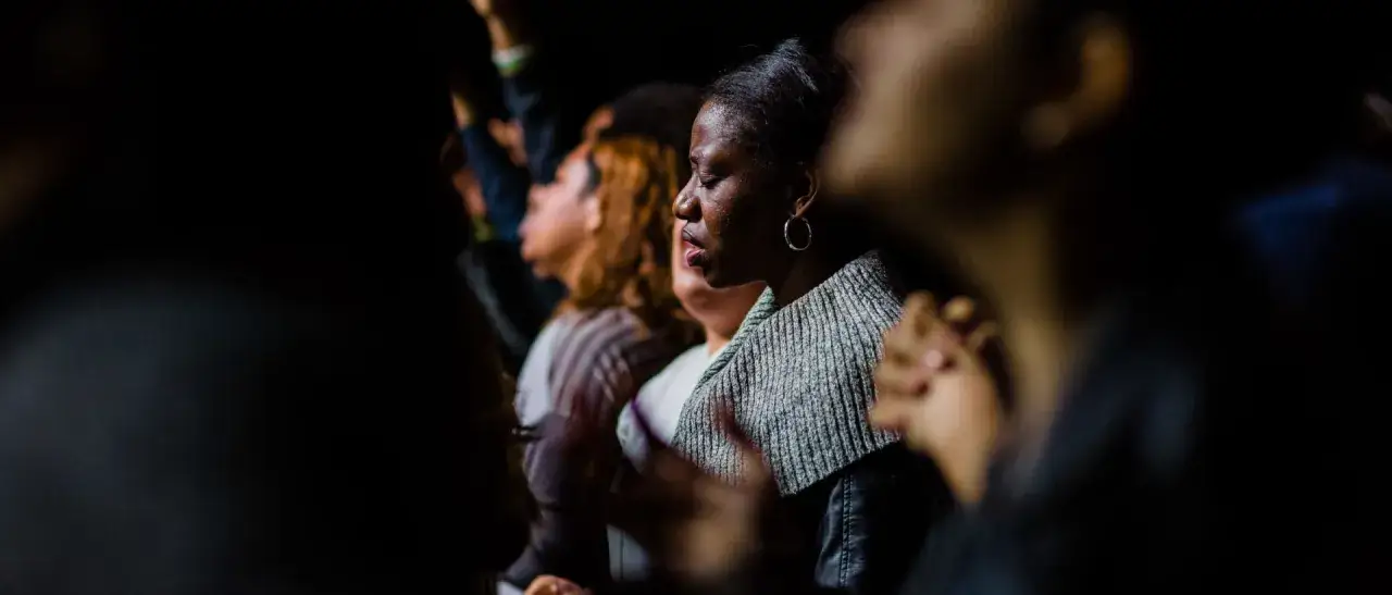 A woman with eyes closed, hands clasped, in a moment of deep prayer. A prayer request is shared in this solemn gathering.