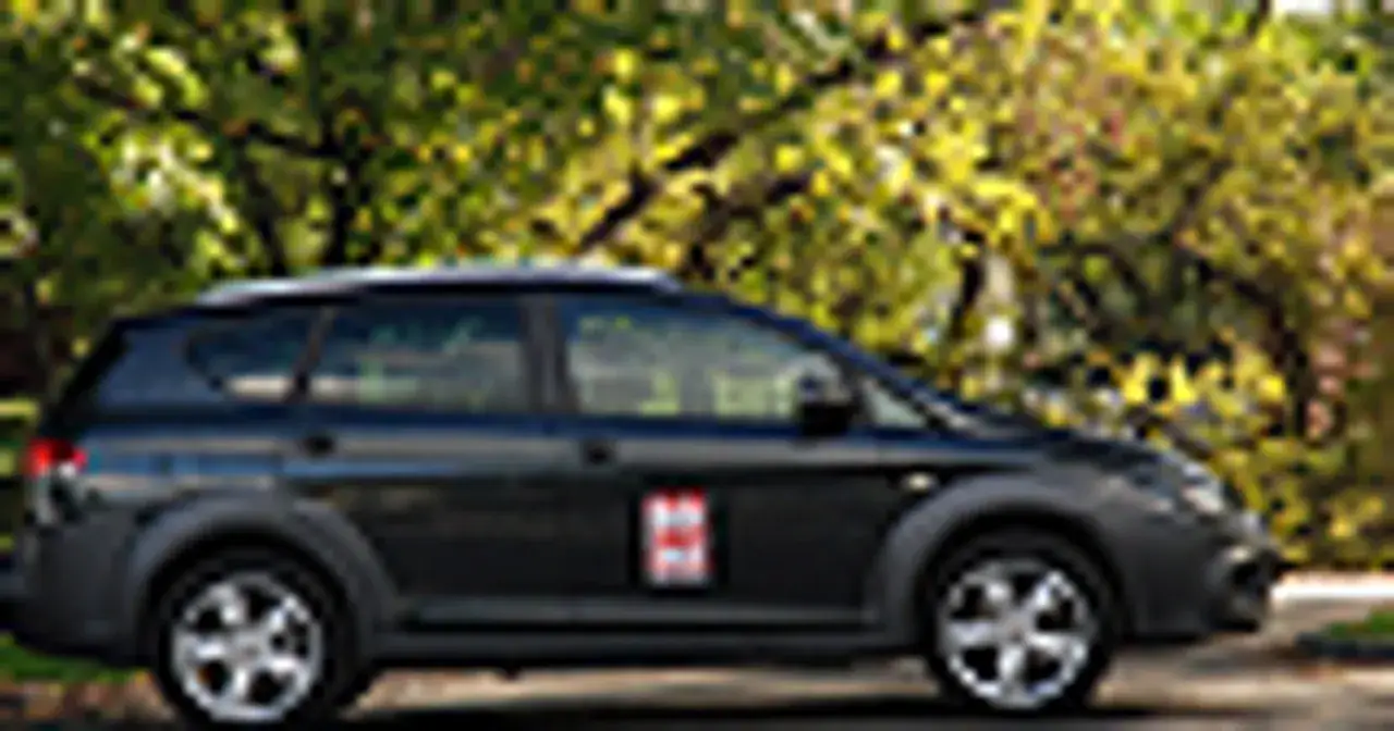 Ciemny Seat Altea XL z charakterystycznym emblematem na drzwiach, zaparkowany na tle jesiennej zieleni.