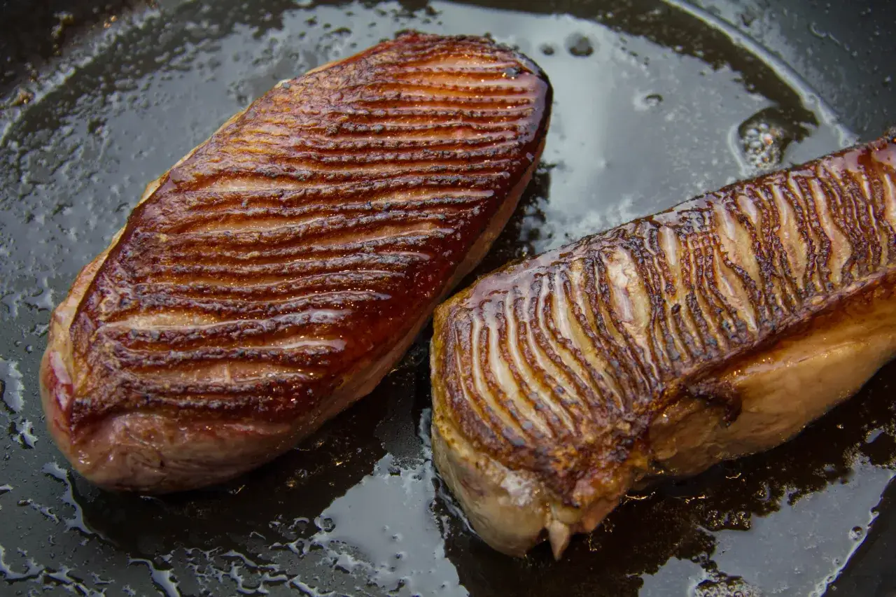 Deux magrets de canard au four, la peau grill&eacute;e et dor&eacute;e, reposent dans une po&ecirc;le avec leur jus.