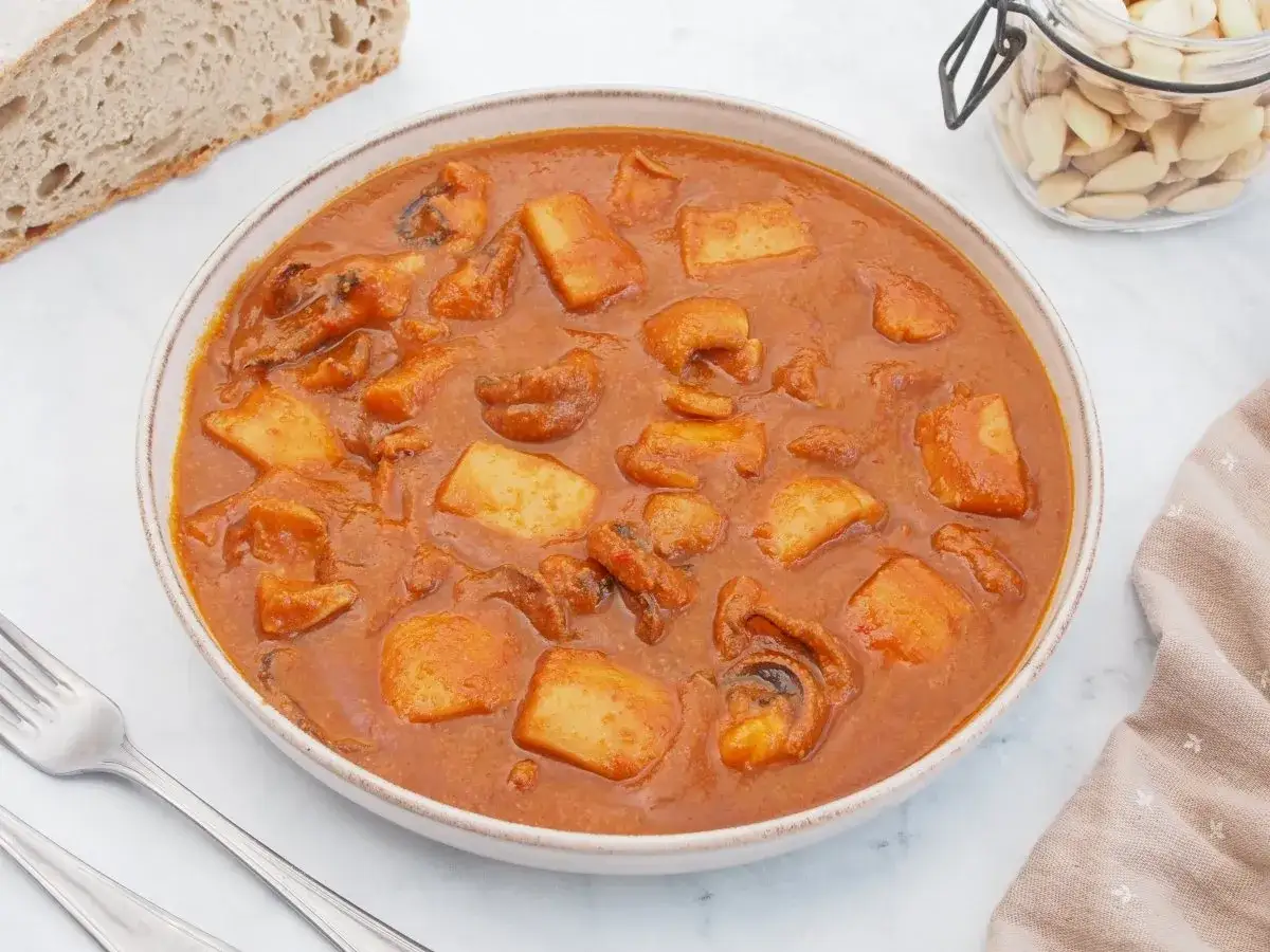 Un plato humeante de jibia en salsa, con trozos de patata y pan r&uacute;stico al lado.