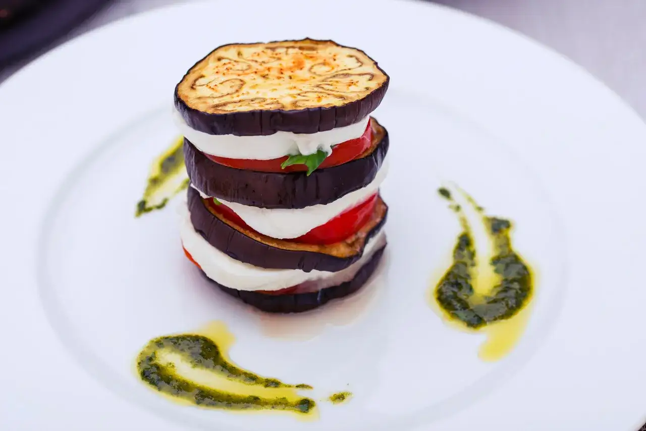 Torretta di melanzane, mozzarella e pomodoro, una gustosa ricetta parmigiana di melanzane non fritte, guarnita con pesto.