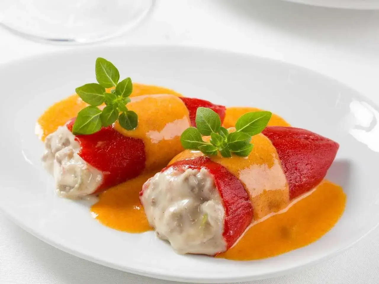 Dos pimientos del piquillo rellenos de carne, cubiertos con una cremosa salsa y decorados con hojas verdes.