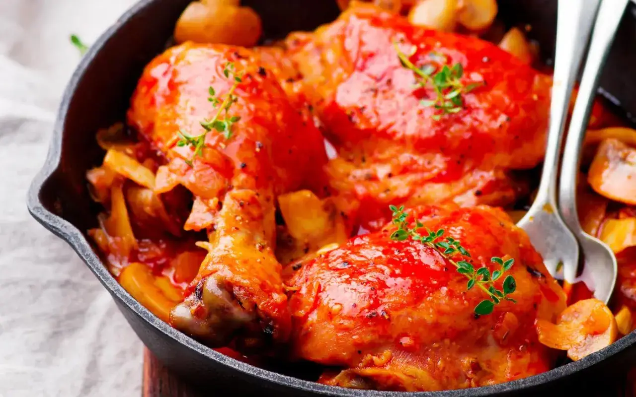 Un savoureux poulet Marengo mijoté dans une sauce tomate riche, garni de thym frais, servi dans une poêle en fonte avec des champignons.