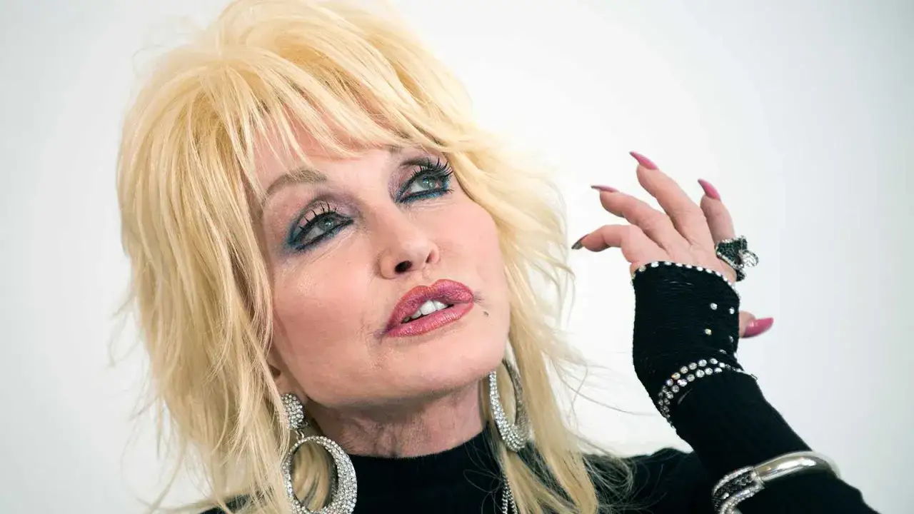 Dolly Parton, trots sin &aring;lder, str&aring;lar med sitt ikoniska blonda h&aring;r och glittrande smycken. Hennes blick &auml;r f&auml;ngslande.