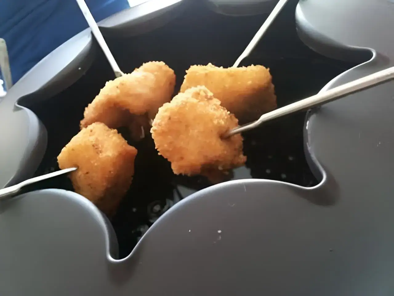 Quatre morceaux de viande blanche panée sur des brochettes, prêts pour une fondue.