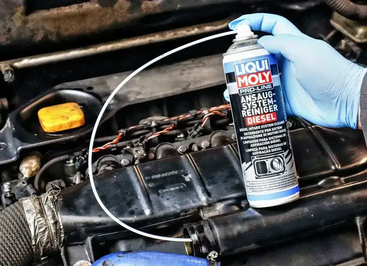 Ręka w niebieskiej rękawiczce aplikuje preparat Liqui Moly do czyszczenia układu dolotowego, aby usunąć nagar i zapobiec zapchaniu EGR.