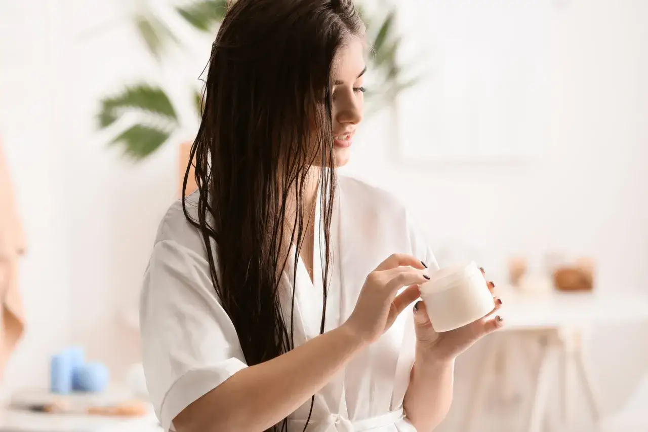 Mujer con cabello mojado y bata blanca, sosteniendo un tarro de crema. Descubre qu&eacute; es el living para el cabello y c&oacute;mo puede transformar tu rutina.
