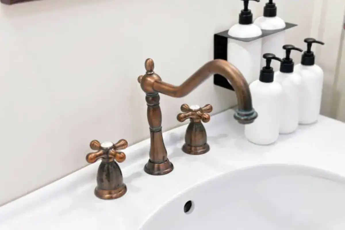 Grifo de bronce antiguo y dispensadores de jab&oacute;n blancos sobre un lavabo. Un toque de elegancia para limpiar bronce.