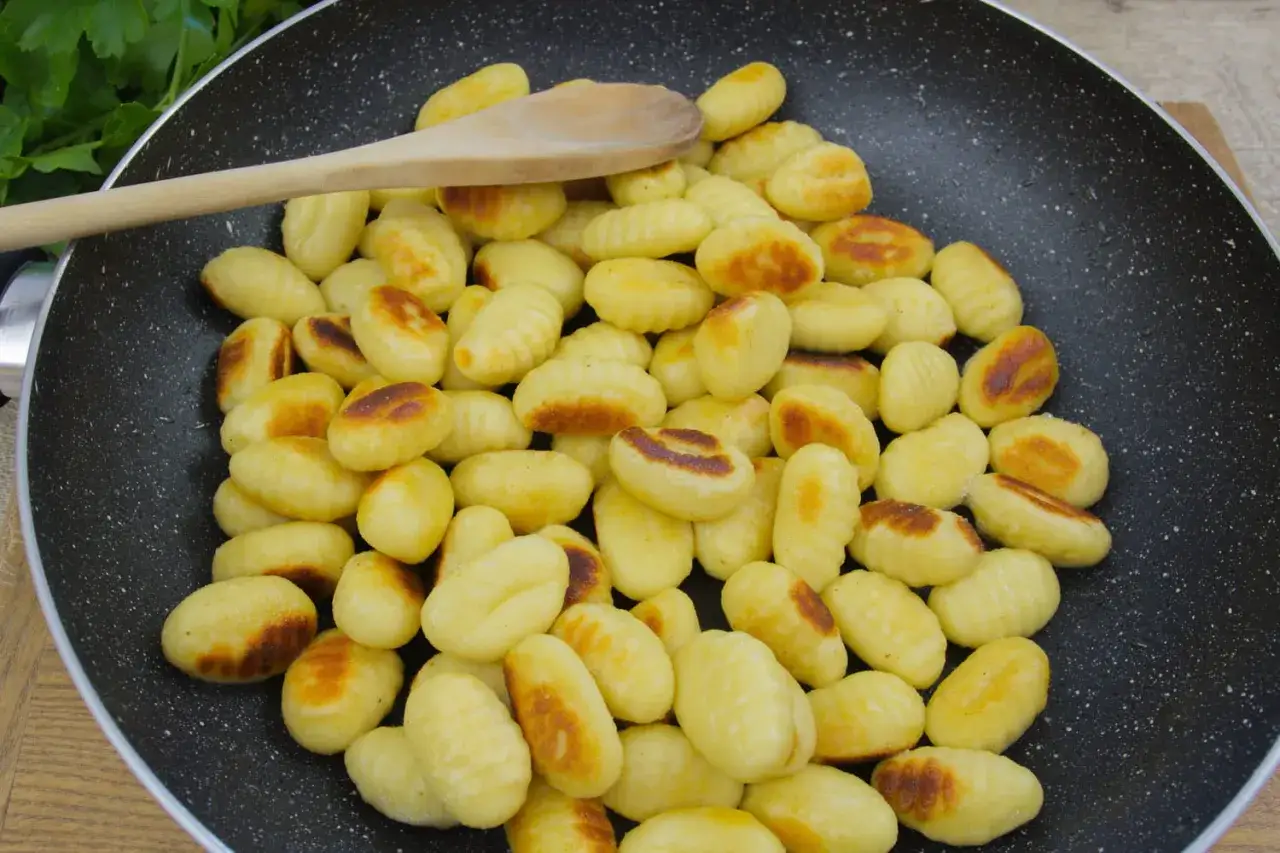 Cuisson gnocchi dans une poêle, avec une cuillère en bois. Ils dorent joliment, prêts à être dégustés.