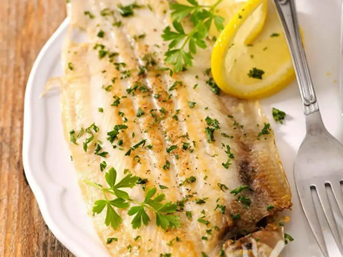 Sogliola al forno, dorata e profumata, guarnita con prezzemolo fresco e spicchi di limone. Un piatto leggero e gustoso.