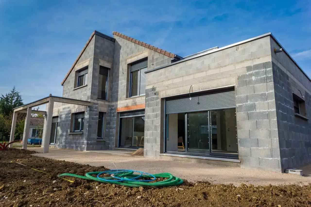 Maison en construction, parpaings apparents, fenêtres avec volets roulants. Le prix d'une maison neuve 100m2 sans terrain est une question clé.