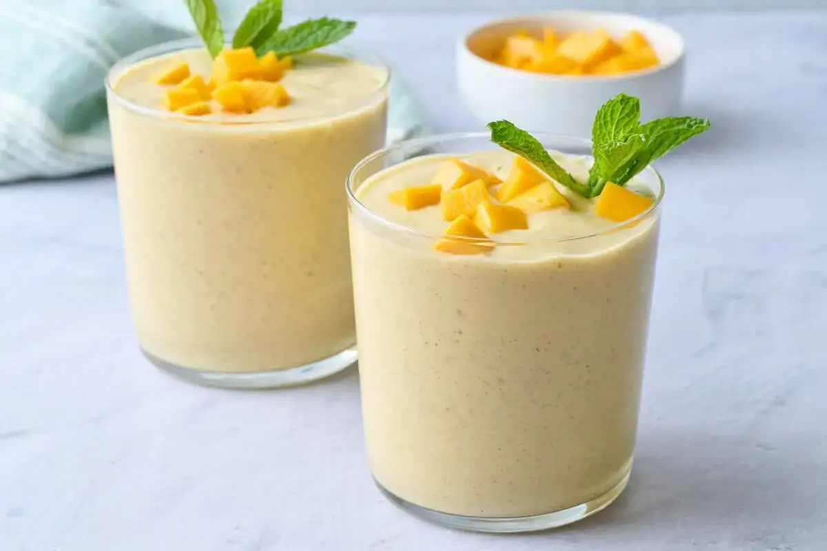 Dwa orzeźwiające koktajle z mango, udekorowane kostkami owocu i listkami mięty, gotowe do spożycia.