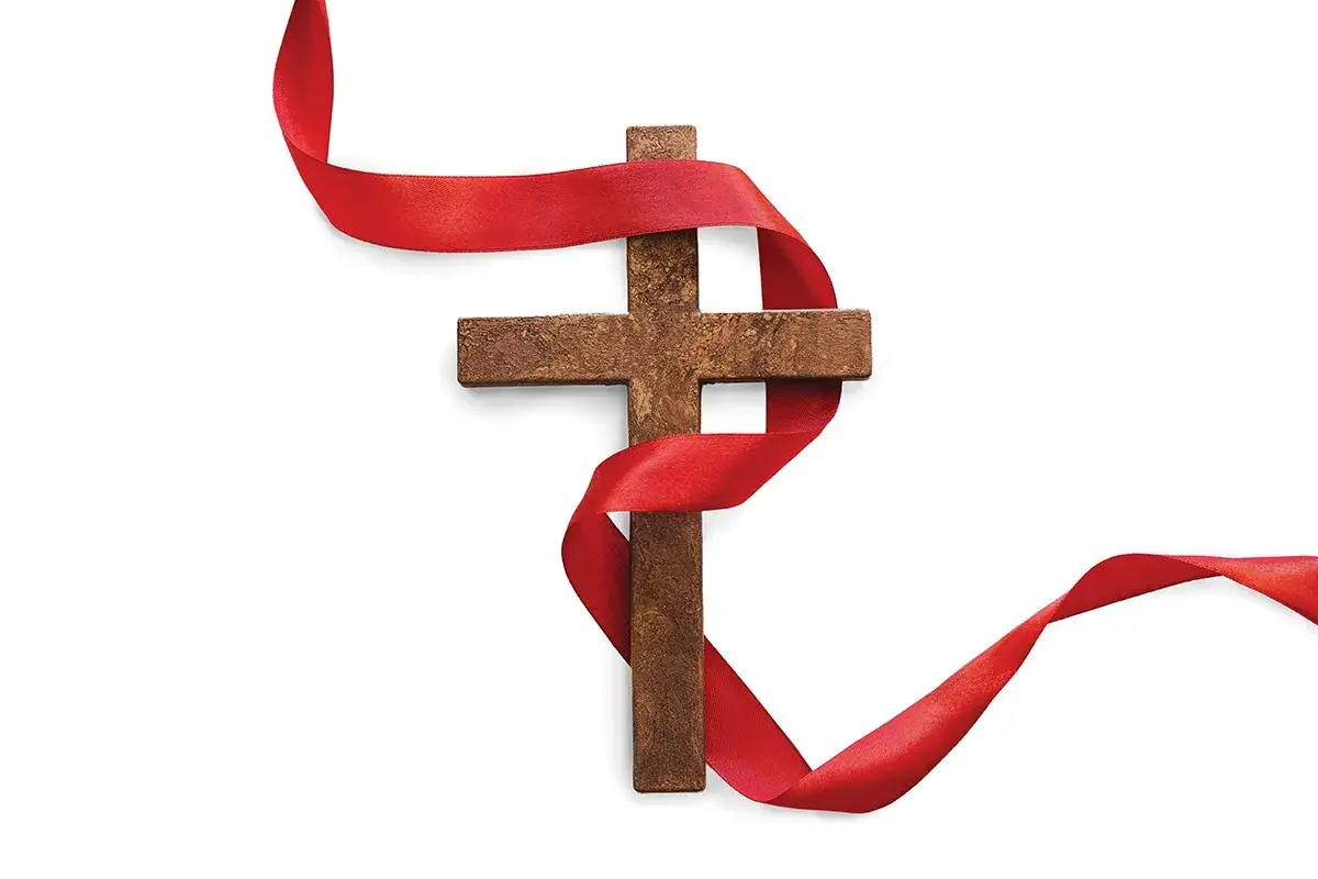 Drewniany krzyż owinięty czerwoną wstęgą, symbolizującą krew Jezusa.