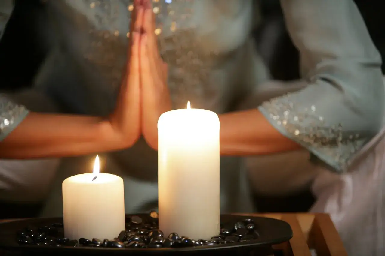 Manos juntas en oraci&oacute;n, dos velas encendidas y piedras negras. Un momento para enviar energ&iacute;a positiva.