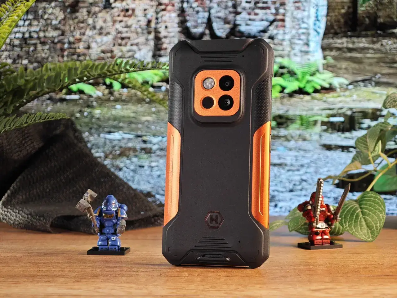 Wytrzymały polski smartfon w otoczeniu figurek żołnierzy i roślinności.