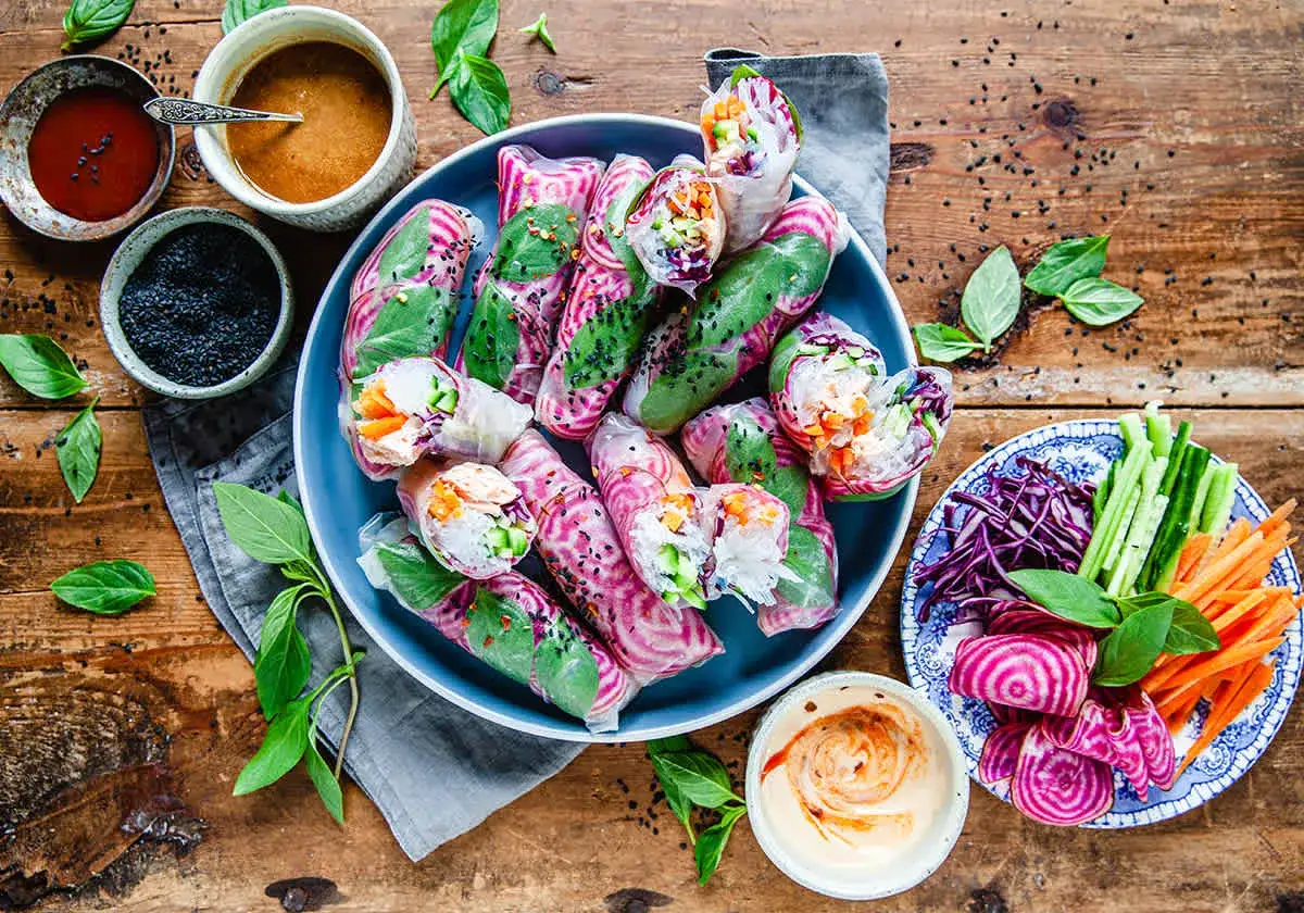 Färska vietnamesiska vårrullar med grönsaker och risnudlar, serverade med dippsåser och extra grönsaker. Perfekt för en lätt och god måltid.