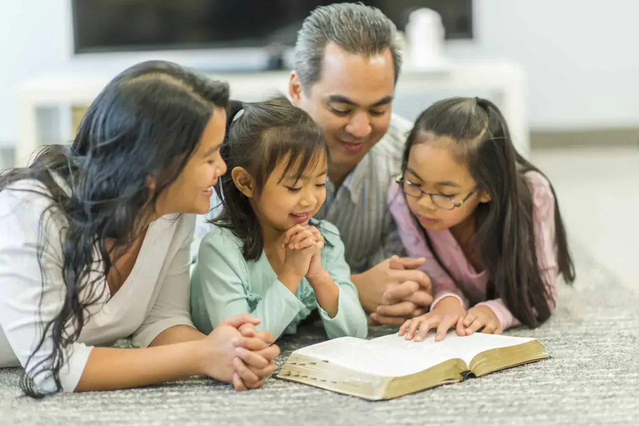 Eine Familie liegt auf dem Boden und liest in der Bibel. Wesley und die Gebete sind Teil ihrer t&auml;glichen Routine.