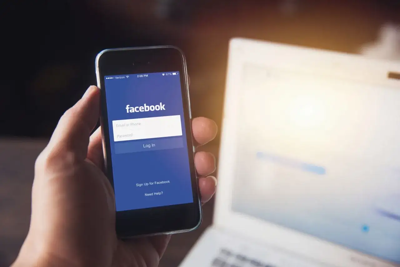 Dłoń trzyma smartfon z ekranem logowania Facebooka. Dowiedz się, jak odblokować aplikacje na Facebooku, wpisując dane logowania.
