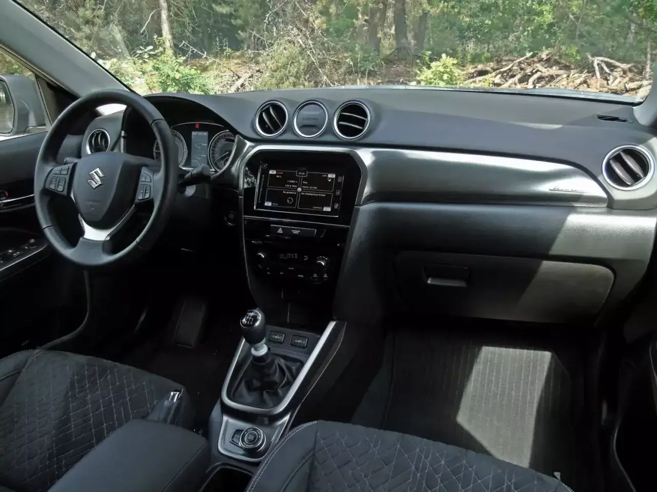 Wnętrze Suzuki Vitara 2023: kierownica, ekran multimedialny, dźwignia zmiany biegów i fotele.