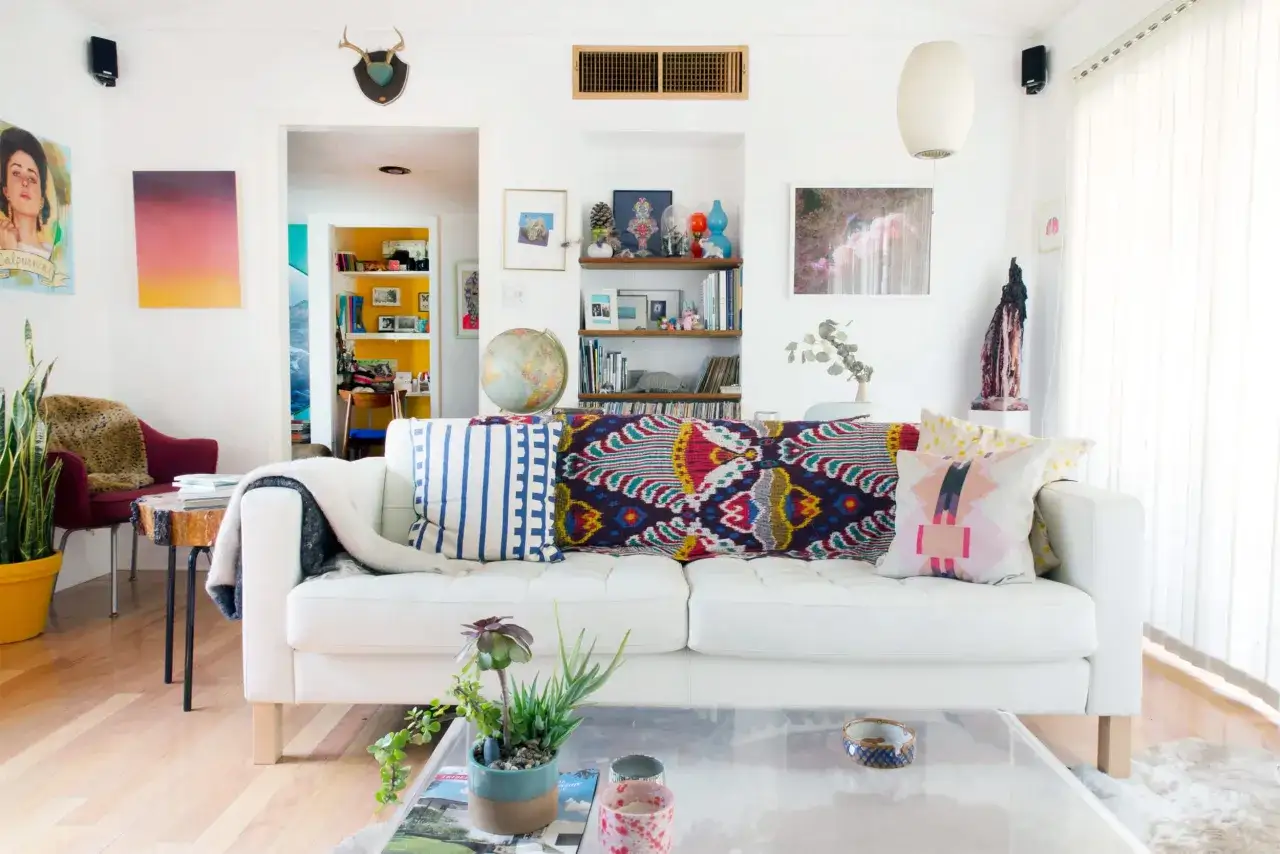 Gemütliches Wohnzimmer mit weißem Sofa, bunten Kissen und Kunstwerken. Perfekt für die erste eigene Wohnung!