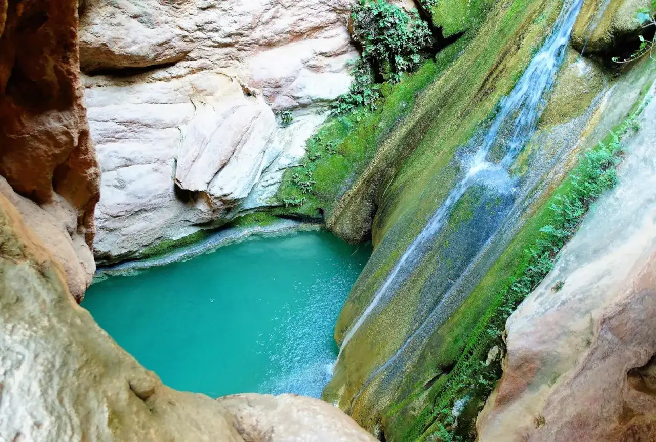 La cascada de Bercolon desciende por una pared rocosa cubierta de musgo hacia una piscina de agua turquesa.