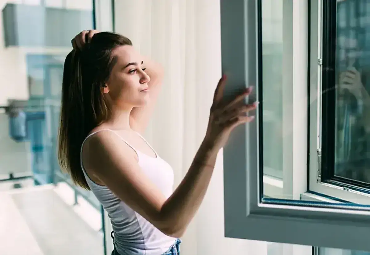 Joven abre una ventana sin obra, disfrutando de la luz y el aire fresco.