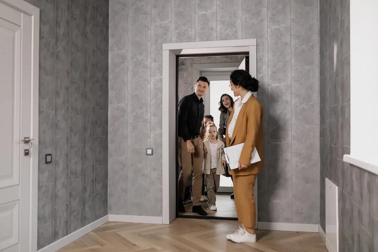 Rodzina wchodzi do nowego domu podczas **open houses**. Agentka nieruchomości wita ich z uśmiechem.