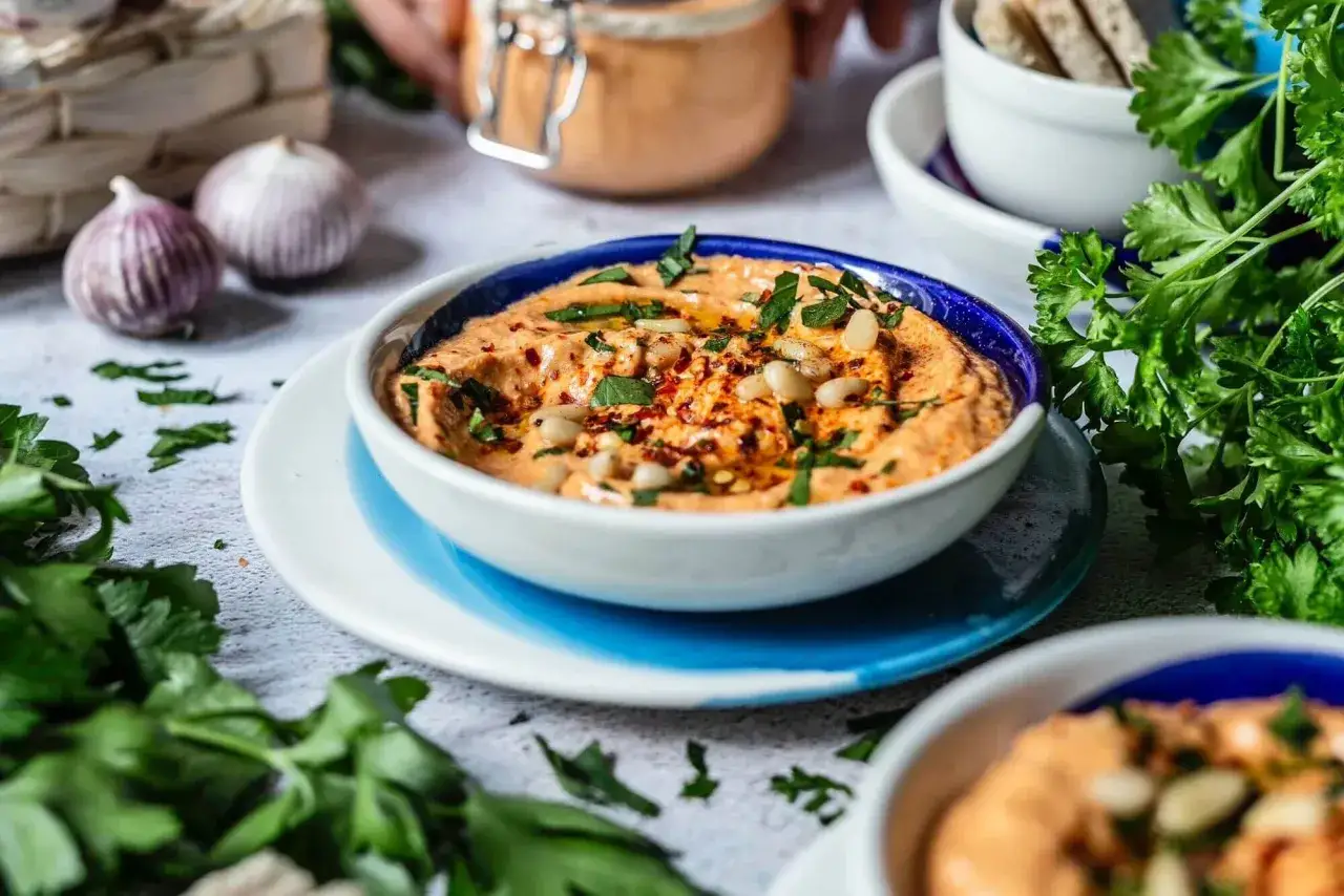 Cremiger Paprika Feta Dip, garniert mit Pinienkernen und Petersilie, bereit zum Dippen.