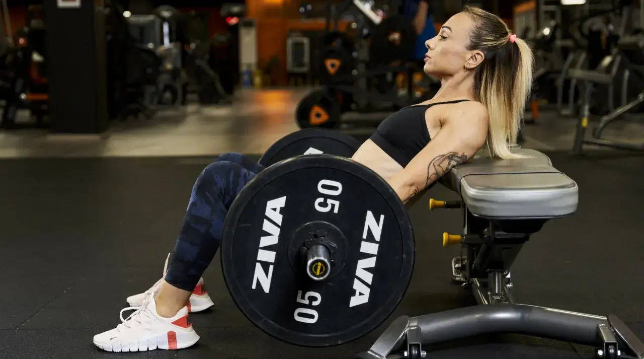 Donna in palestra esegue hip thrust con bilanciere, allenando i glutei perfetti.