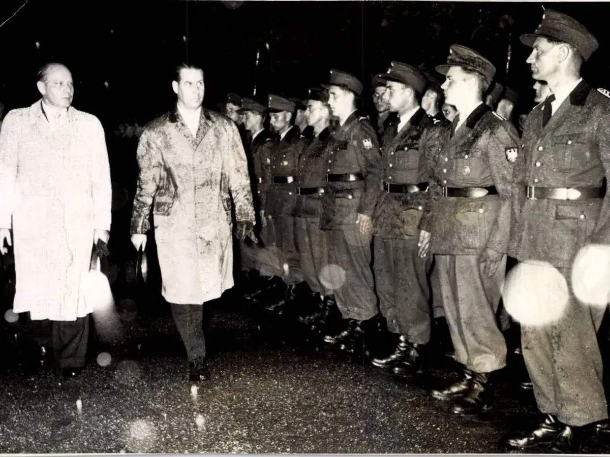 Zwei M&auml;nner in M&auml;nteln gehen an einer Reihe von Soldaten der Bundeswehr vorbei. Ein historischer Moment, der an Bundeswehr Zitate erinnert.
