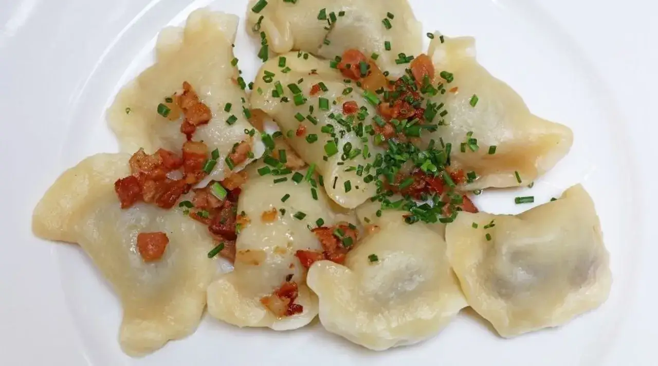 Pyszne pierogi z mięsem z rosołu, posypane skwarkami i szczypiorkiem, na białym talerzu.