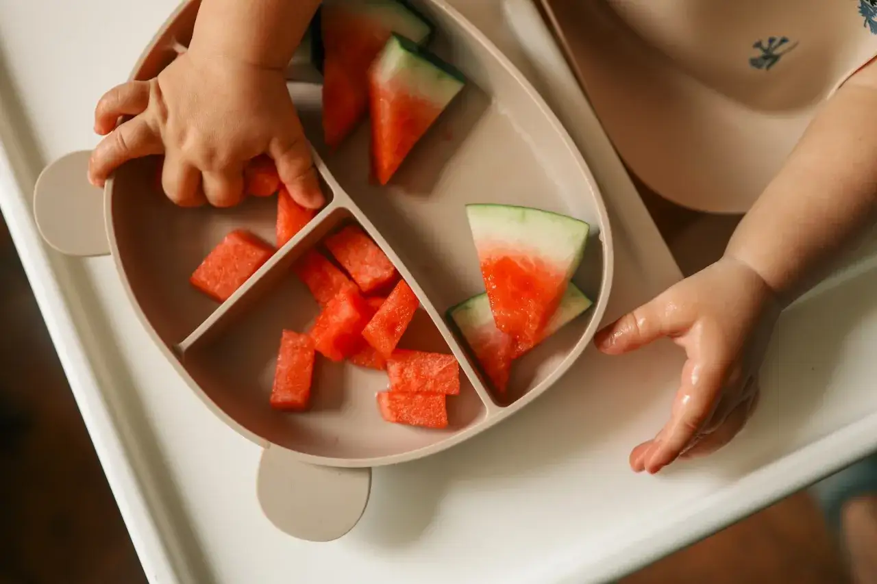 Kleine Hände greifen nach saftigen Wassermelone-Stücken auf einem Teller. Ein süßer Wassermelone-Baby-Moment.