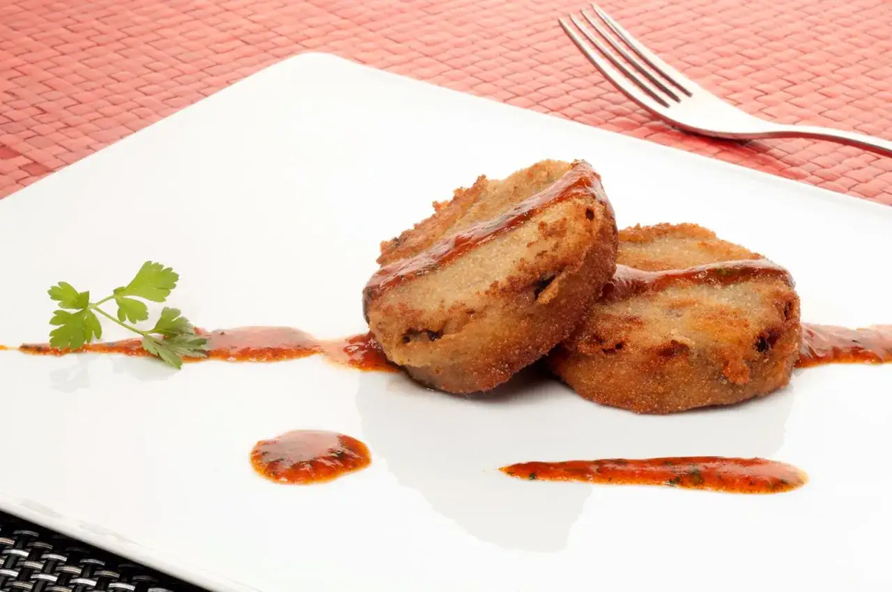Dos manitas de cerdo rebozadas y fritas, servidas con salsa roja y perejil en un plato blanco.