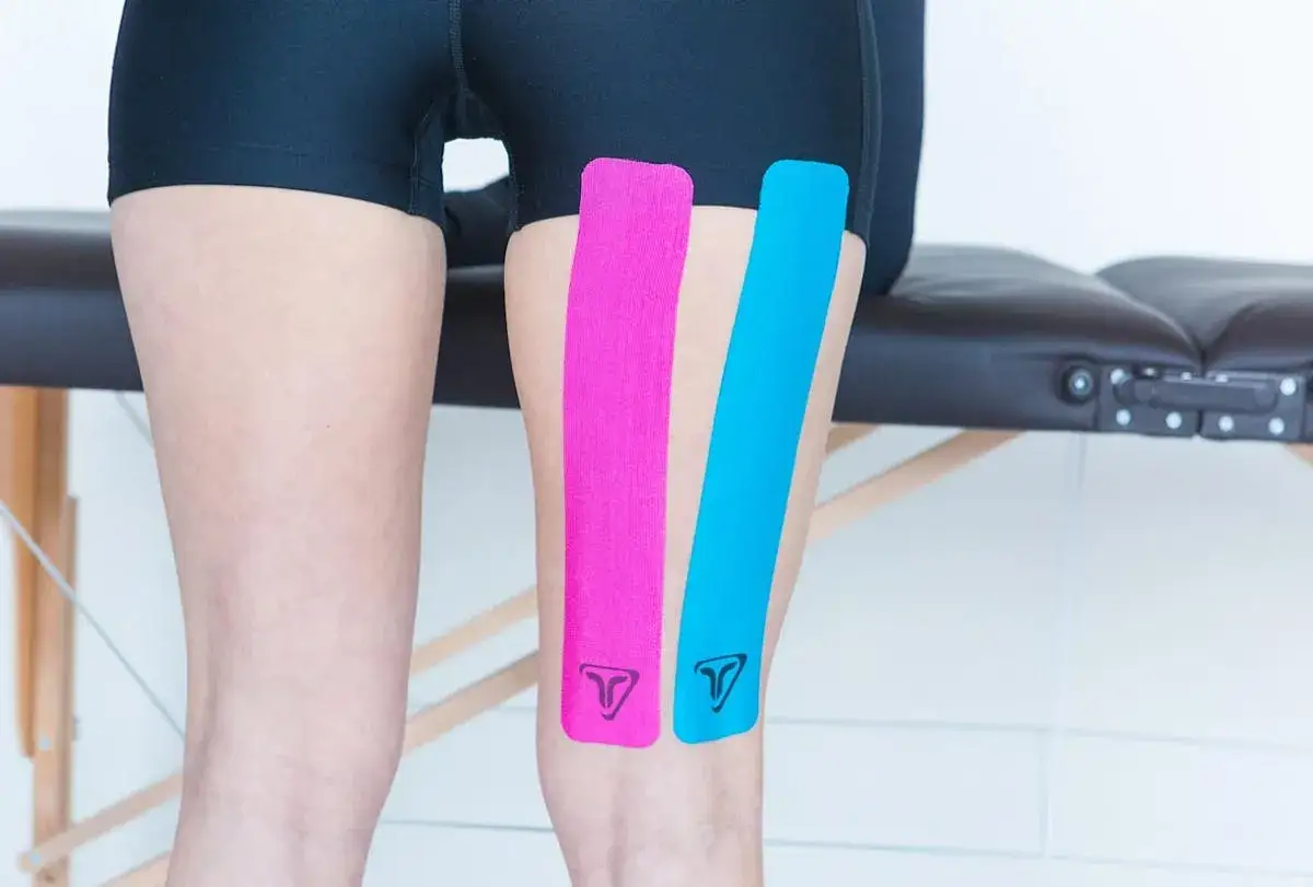 Bandes de kinésiologie rose et bleue appliquées sur le quadriceps d'une personne, prêtes pour le sport.