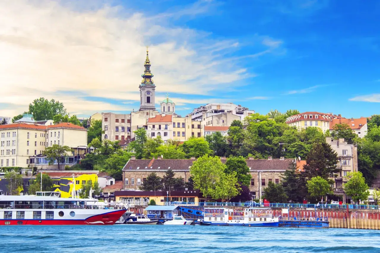 Widok na Belgrad z rzeki, idealne miejsce na serbiańskie wakacje. Statki cumują przy brzegu, a w tle widać zabytkowe budynki i kościelną wieżę.