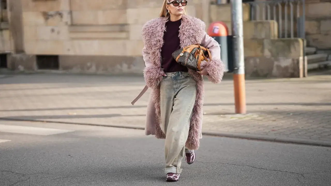 Mujer con abrigo rosa peludo, vaqueros anchos y zapatillas deportivas, luciendo un bolso de dise&ntilde;ador.