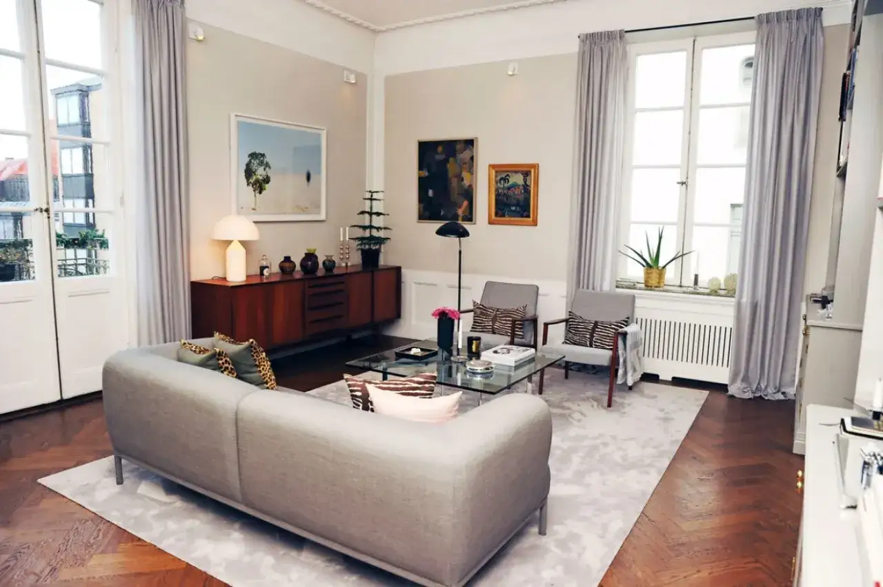 Ett modernt vardagsrum med en gr&aring; soffa, glasbord och konstverk p&aring; v&auml;ggen. Johan Pr&aring;mell skulle trivas h&auml;r.