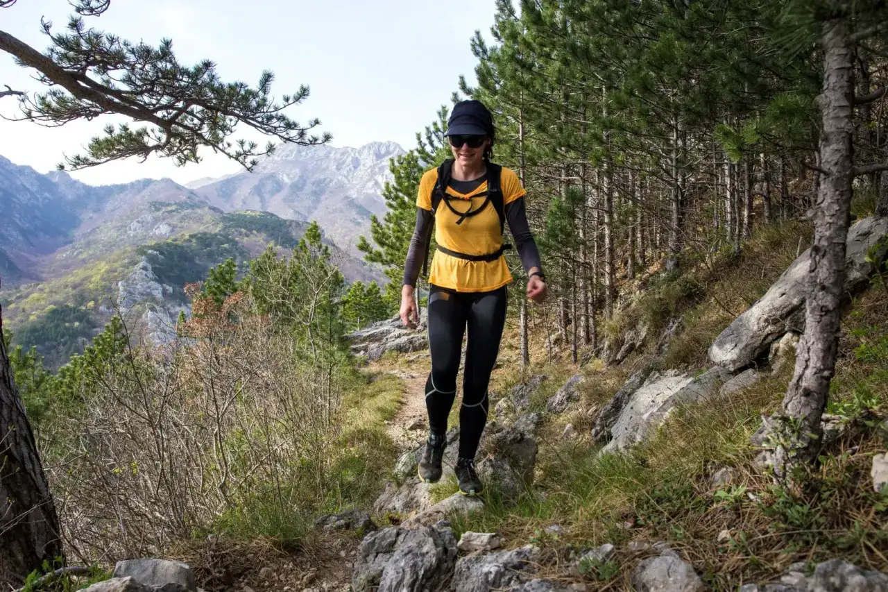 Woman hiking on a rocky trail through a pine forest, enjoying Croatia hiking trips with stunning mountain views.