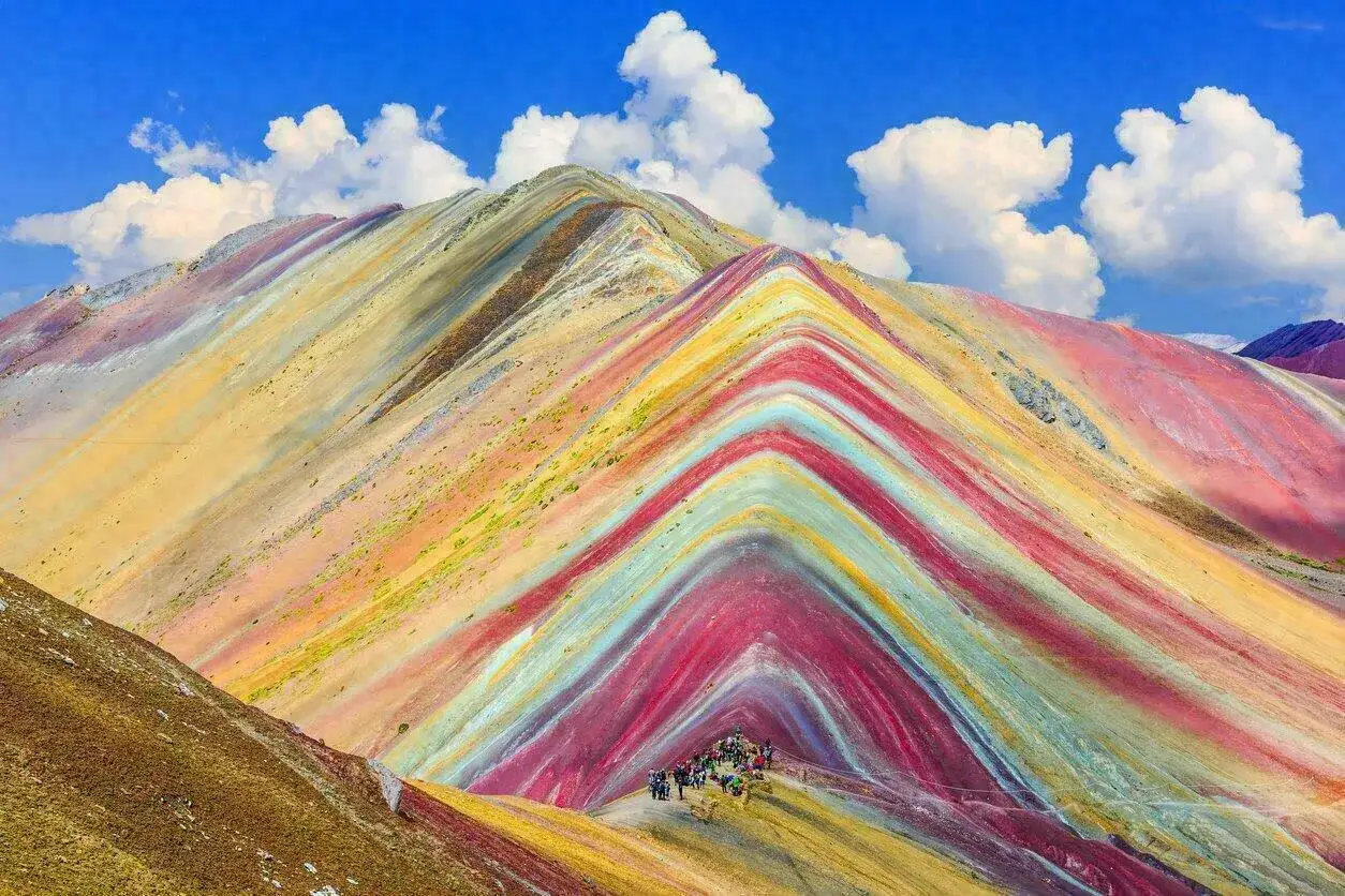 La montagne Vinicunca, aux couleurs vives, dévoile ses strates minérales sous un ciel bleu parsemé de nuages.