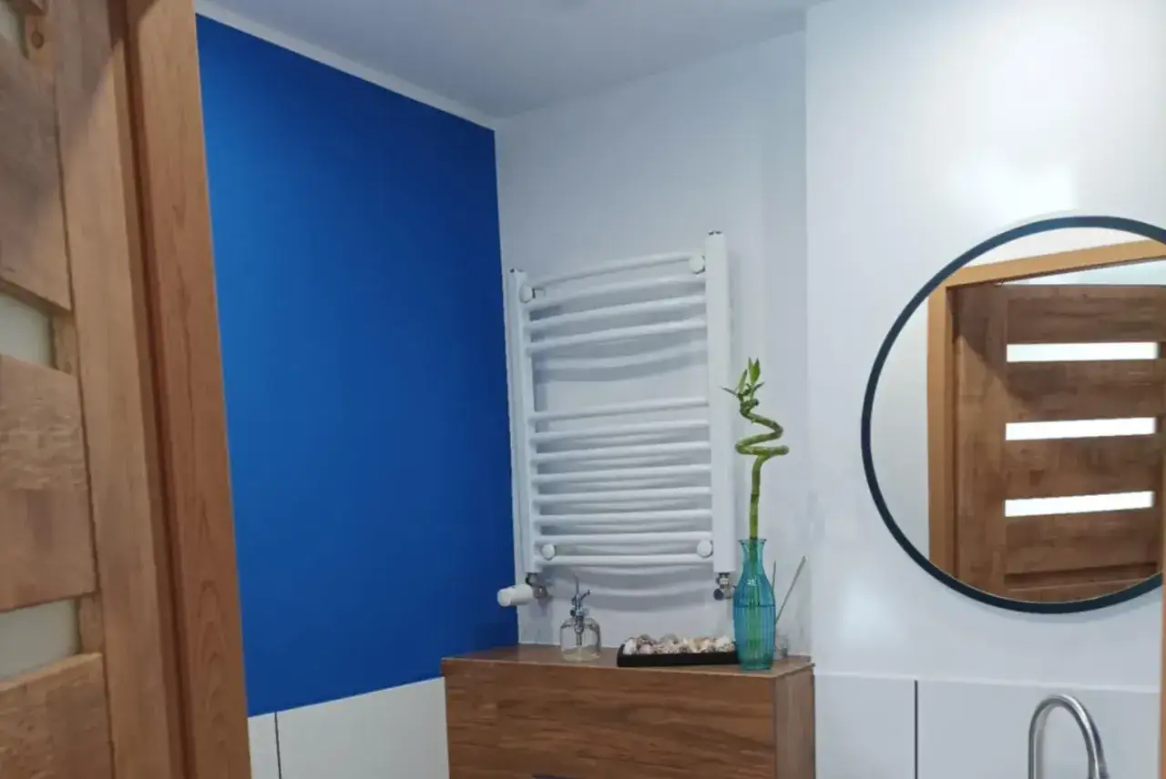 Łazienka z akcentem **cobalt blue** na ścianie, drewnianymi drzwiami i okrągłym lustrem.