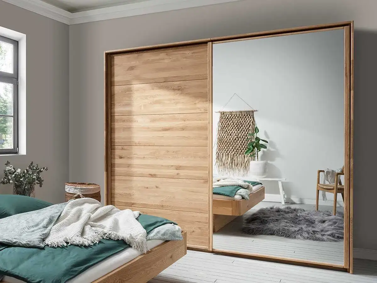 Holzschrank mit Spiegelt&uuml;r, eine tolle Idee f&uuml;r Ihr Ankleidezimmer. Ein Bett mit gr&uuml;ner Bettw&auml;sche und Decken steht daneben.