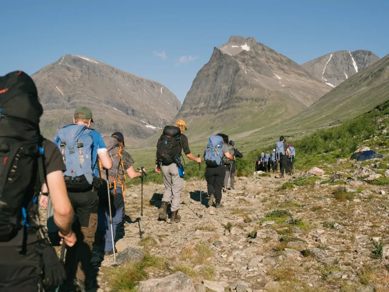 Vandrare på väg mot Kebnekaise, Sveriges högsta berg. Solen skiner över fjällandskapet.