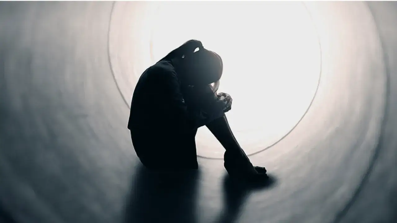 Silhouette di persona rannicchiata in un tunnel, simbolo di solitudine e mancanza di affetto. La luce in fondo al tunnel offre un barlume di speranza.