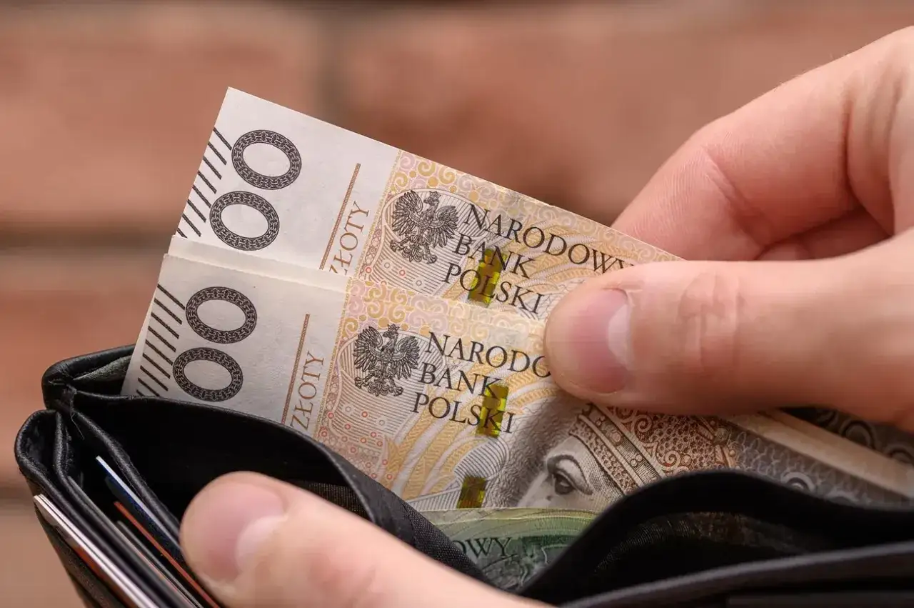 Dłoń wkłada do portfela banknoty 100 zł. Może to być dodatek do emerytury po 75 roku życia, zapewniający komfort.