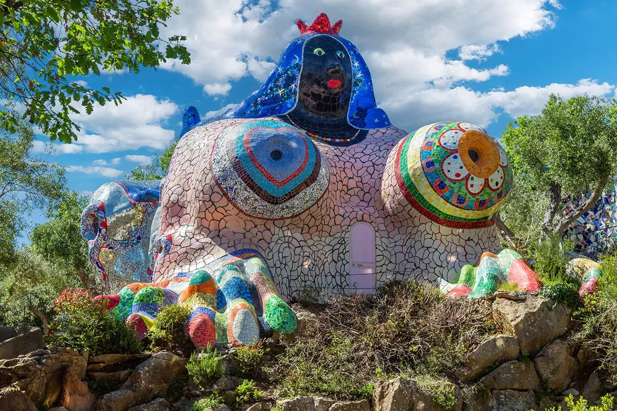 La Grande Matriarca, un'opera del Giardino dei Tarocchi, accoglie con le sue forme sinuose e i mosaici colorati sotto un cielo azzurro.