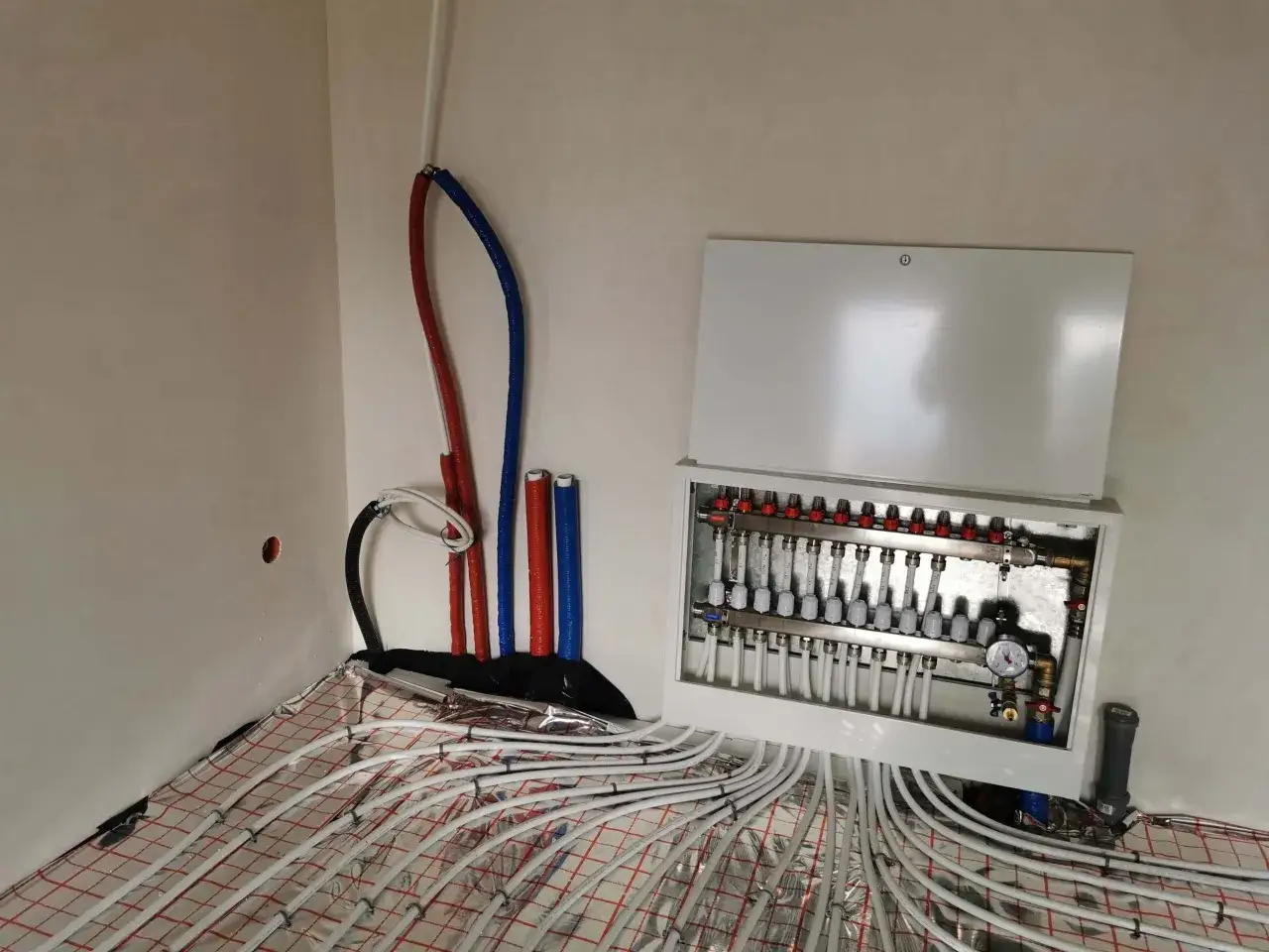 Płukanie instalacji podłogówki. Rozdzielacz i rury systemu grzewczego gotowe do pracy. Sprawdź cennik usług.