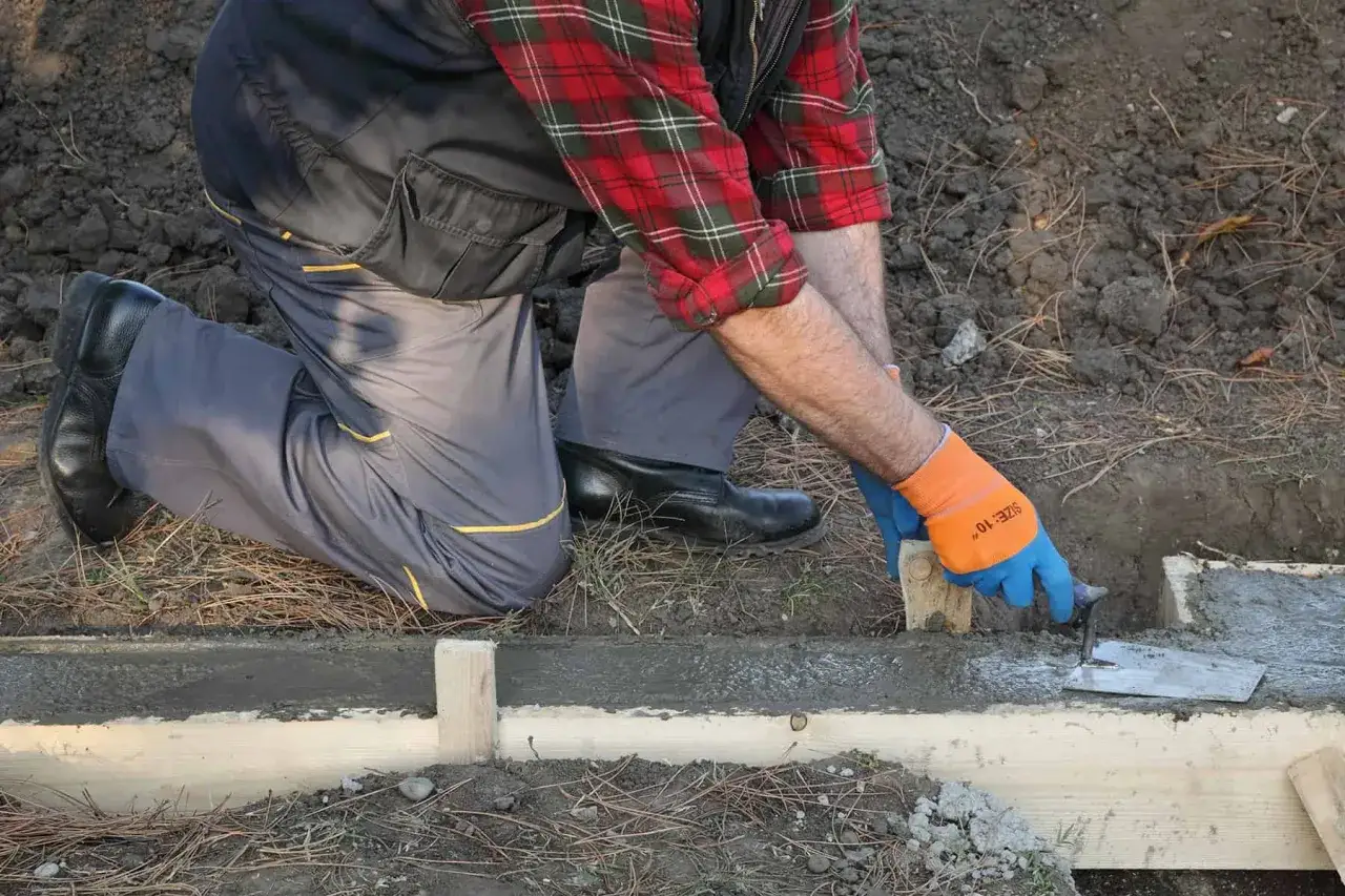 Pracownik w rękawiczkach i kratę wygładza beton. Zastanawiasz się, ile kosztuje płot betonowy?