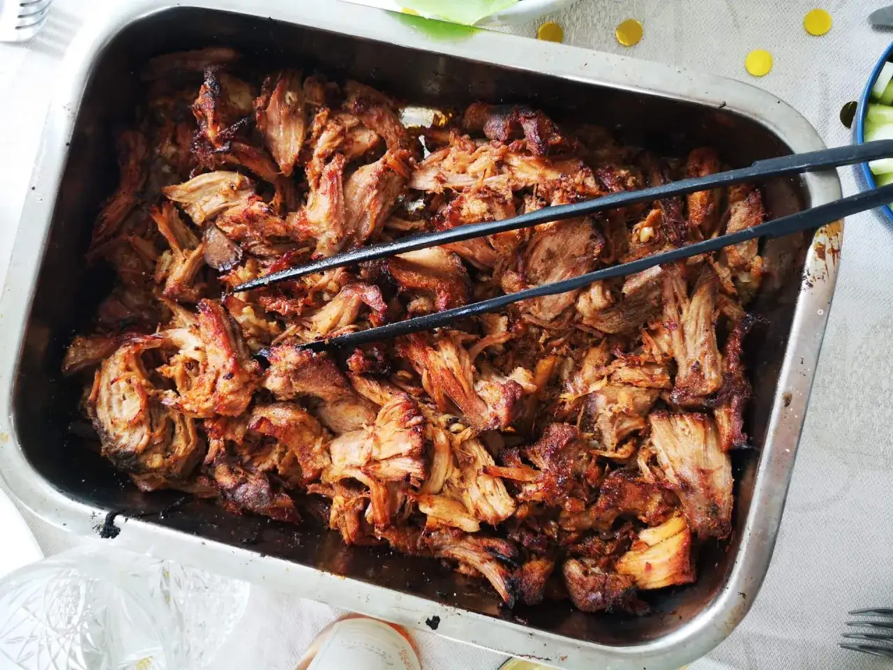 Saftigt, strimlat fläskkött i en ugnsform, redo att serveras. Perfekt för ett enkelt carnitas recept.