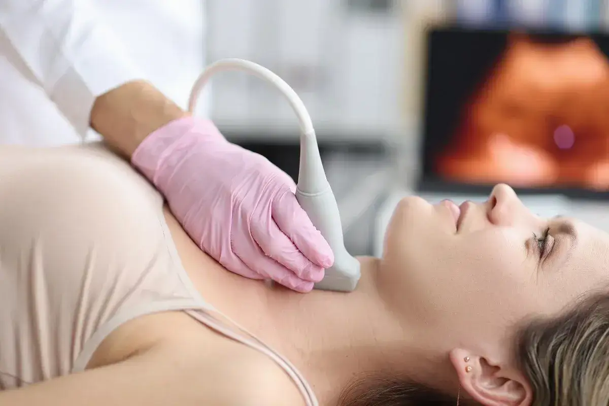 Lekarz wykonuje biopsję cienkoigłową tarczycy pacjentki, używając sondy USG. Na ekranie widoczny obraz diagnostyczny.