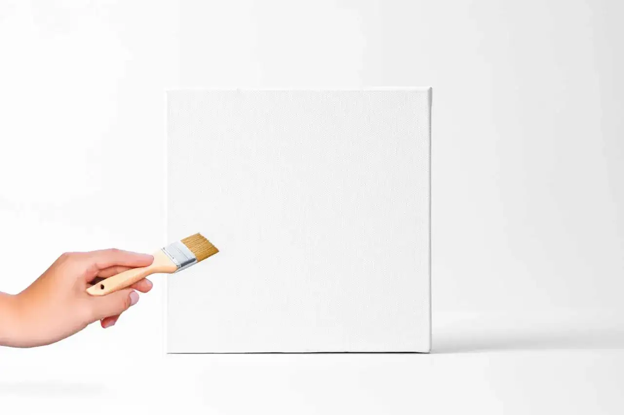 Une main tient un pinceau prêt à peindre une toile blanche immaculée, symbole de créativité et de nouvelles possibilités.